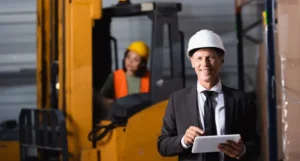 Inspektor w kasku z tabletem nadzorujący procesy i kontrolę jakości na hali produkcyjnej.