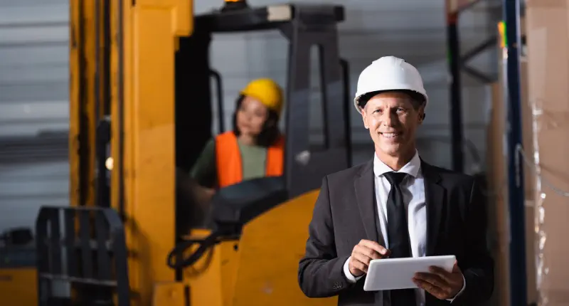 Inspektor w kasku z tabletem nadzorujący procesy i kontrolę jakości na hali produkcyjnej.